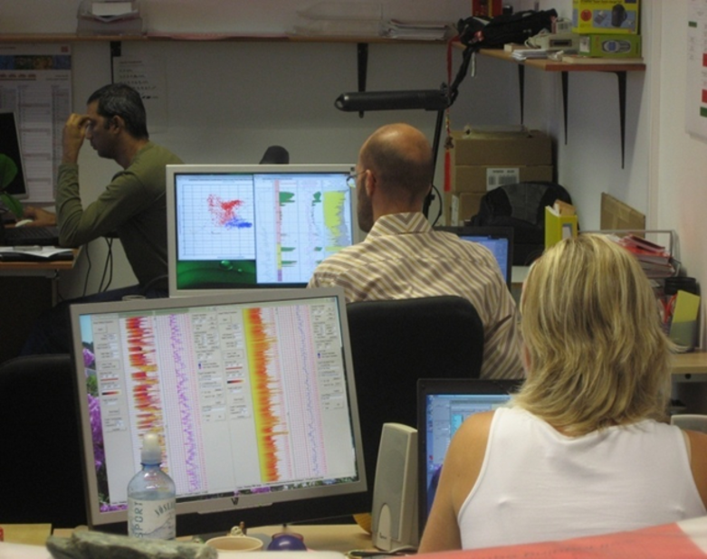 Geologists working in an analysis center performing well log interpretation and reservoir evaluation using advanced logging software
